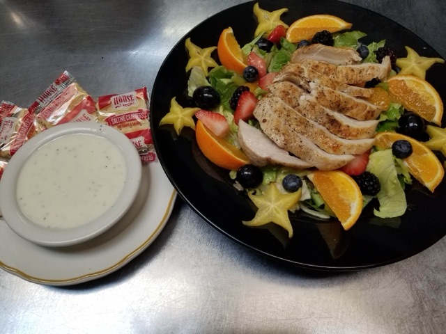 Mixed greens with sliced grilled chicken, orange wedges, berries and star fruit, beside a cup of house dressing and saltines