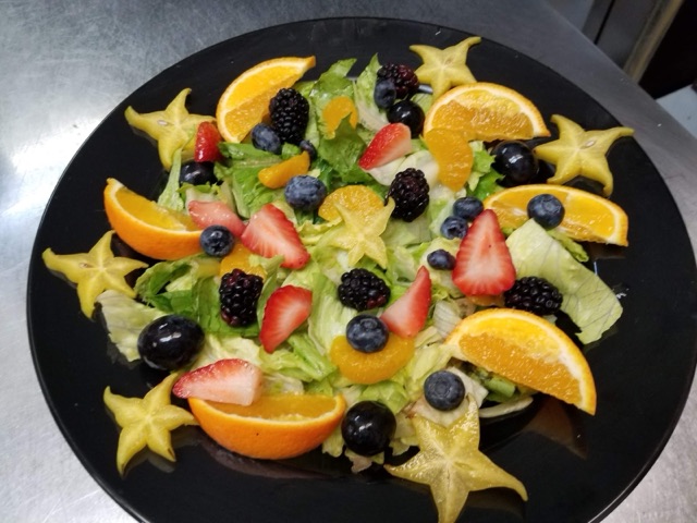 A plate of mixed greens topped with orange wedges, strawberries, blueberries, blackberries and star-fruit slices